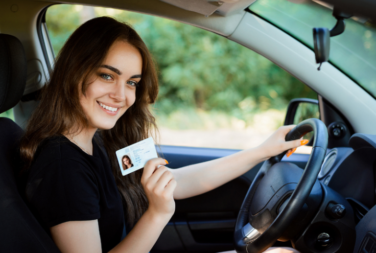 Image is of a happy young woman sitting in the driver's seat of a car, while holding up her driver's license, concept of regaining driver's license after a DUI