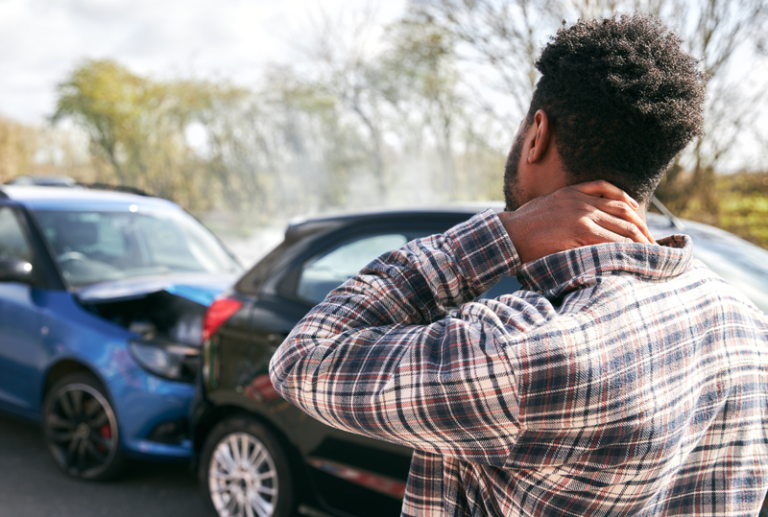 Image is of a man holding his neck in pain following a car accident, concept of how fault is determined in a personal injury case.