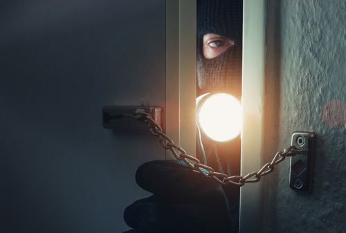 Image is of a home instruder peeking through a doorway with a mask on, concept of stand your ground law in South Carolina