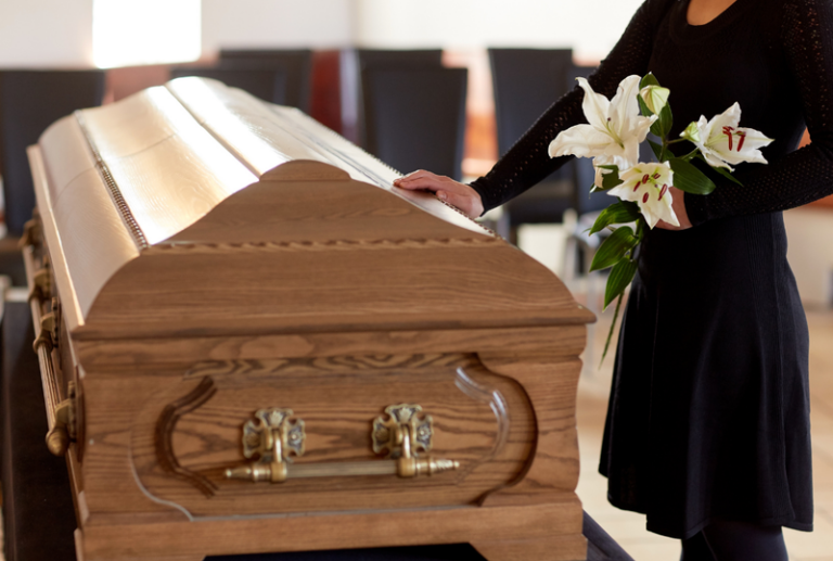 Woman holding flowers with her hand on a casket at a funeral for a loved one concept of wrongful death claims in South Carolina