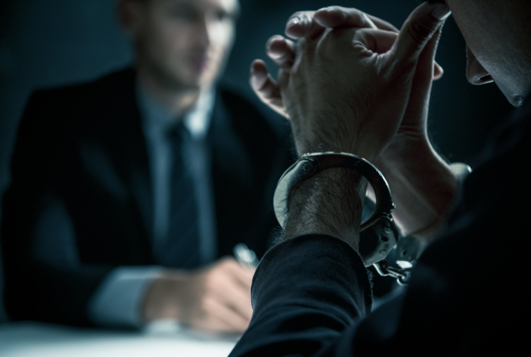 Image is of a person in handcuffs, speaking to a criminal defense lawyer