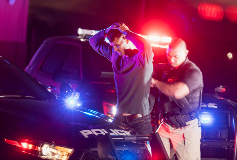 Image is of a man being arrested by a police officer at night, concept of falsely accused of crime