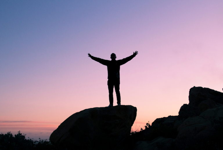 Image is of a silhouette of a person standing on a rock in the mountains against a blue and purple sky, concept of personal and legal recovery of a DUI