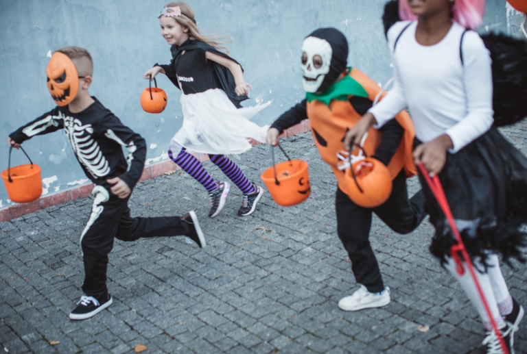 Image is of a group of young kids in Halloween costumes running down a street while trick-or-treating, concept of ways to avoid a personal injury on Halloween