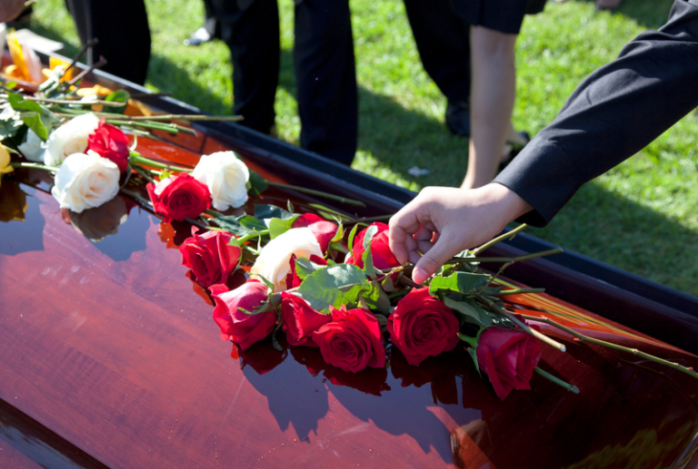 Image is of a coffin at a gravesite with red and white roses on top of the coffin, concept of wrongful death claims in South Carolina