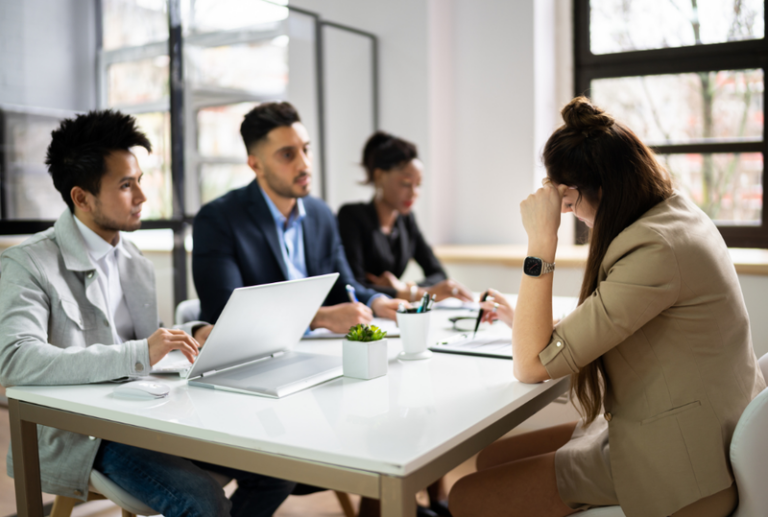 Image is of an upset woman sitting at a table with upper management, concept of professional license suspension