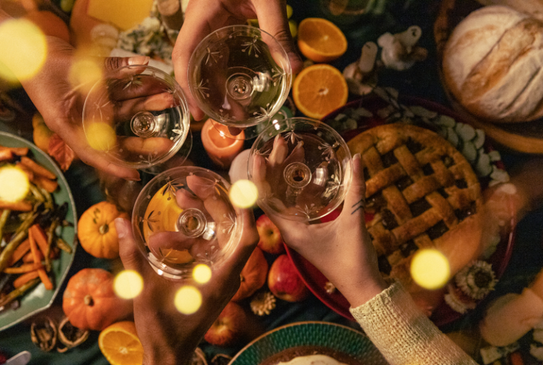 Image is an overhead view of a Thanksgiving dinner with people toasting each other, concept of common Thanksgiving accidents and how to prevent them