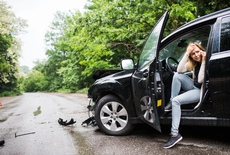 Image is of a distressed woman after a car accident while sitting in her wrecked car, concept of what to do when an at-fault driver has no insurance