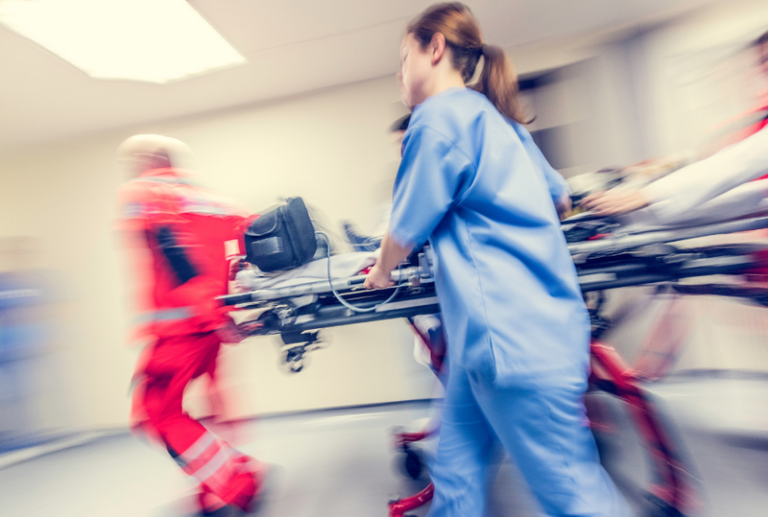 Image is of a team of emergency workers bringing in a patient on a gurney in a hurry, concept of a catastrophic injury