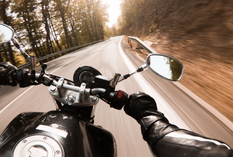 Image is from the point of view of a motorcycle rider driving down a road with lots of trees on either side, concept of do I need a lawyer for a motorcycle accident?