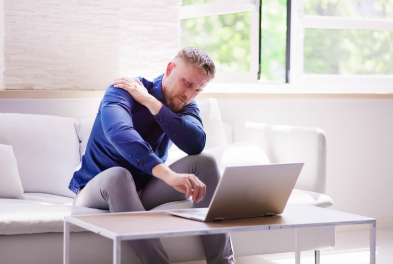 Image is of a man holding his shoulder in pain while using his laptop, concept of how do I know if I have a personal injury case?