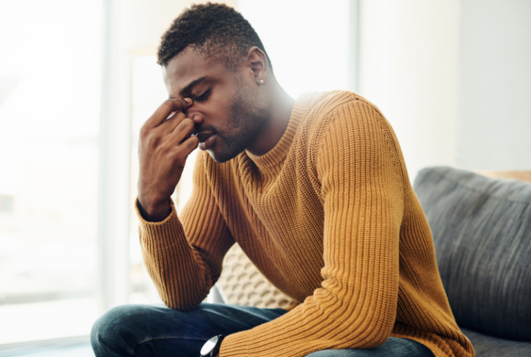 Image is of a man wearing an orange sweater with his hand on his head, concept of can I sue for emotional distress after an accident?