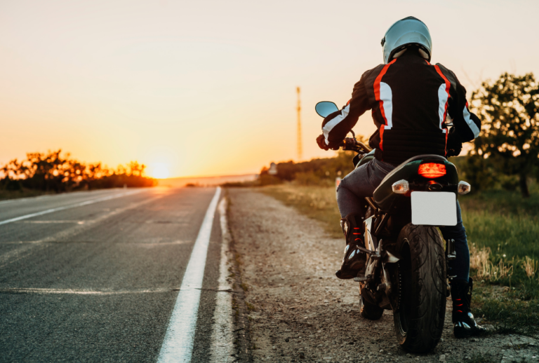 Image is of a motorcycle rider sitting in his bike on the side of a long, deserted road as the sun is setting, concept of motorcycle license requirements in South Carolina