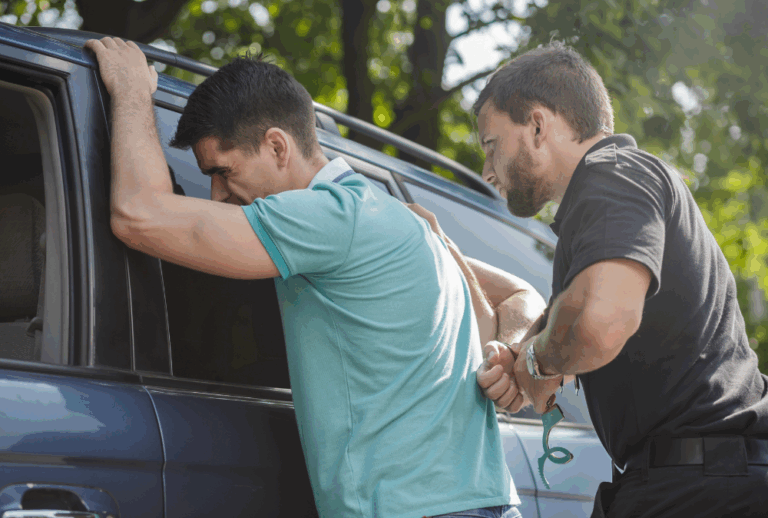 Image is of a man being handcuffed behind his back by a police officer, concept of what to expect after a DUI arrest in Aiken