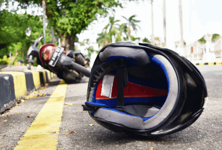 Image is of a motorcycle on it's side on a sidewalk and in the forefront of the image is a motorcycle helmet in the road, concept of what to do after a hit and run motorcycle accident in Aiken