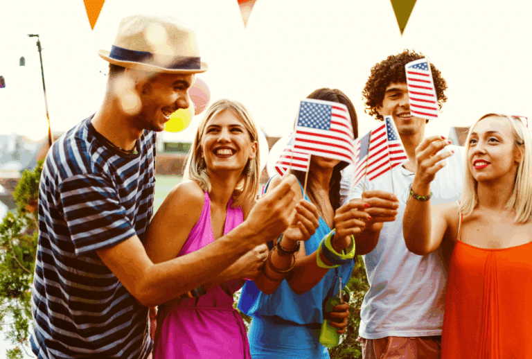 Image is of a group of young adults holding American flags at a party, concept of hosting a safe 4th of July party in Aiken