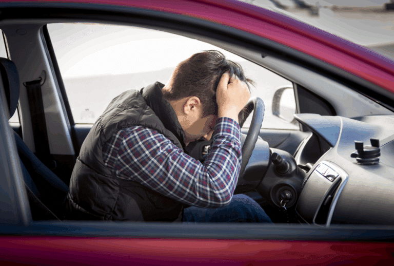 Image is of an upset man with his head on the steering wheel of his car, concept of losing driver's license after a DUI in Aiken