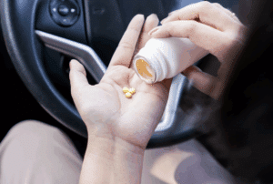 Image is of a woman pouring pills from a bottle into her hand while seating in her car, concept of prescription drug DUI in Aiken
