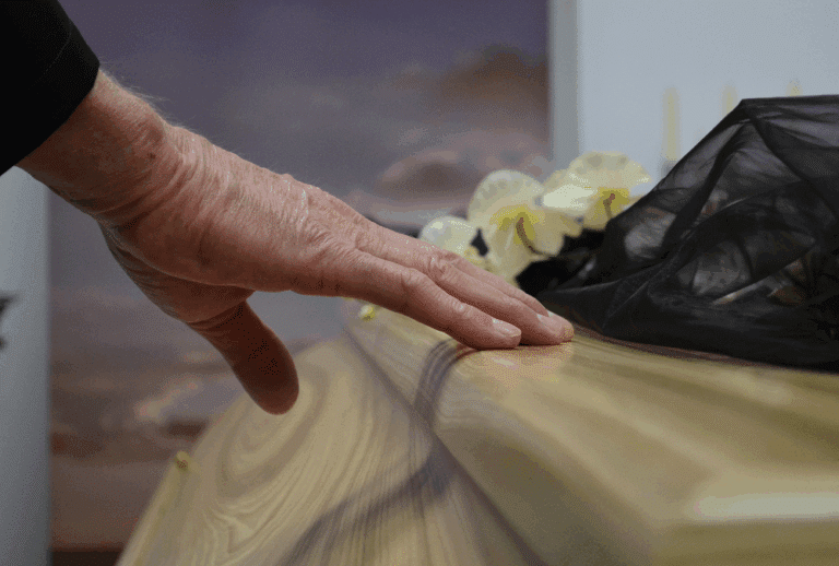 Image is of an older person's hand reaching out to a casket, concept of how wrongful death differs from criminal charges