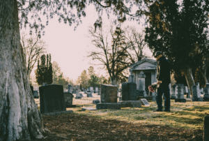 Image is of a man standing at a headstone and placing flowers in a graveyard, concept of compensation in an Aiken wrongful death case
