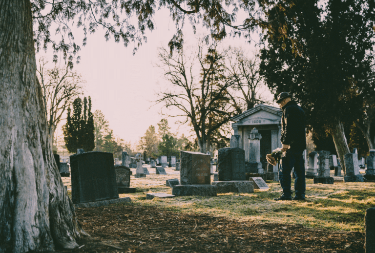 Image is of a man standing at a headstone and placing flowers in a graveyard, concept of compensation in an Aiken wrongful death case