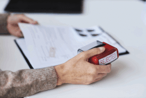 Image is of a closeup of a woman using a stamp on a claim that reads 'denied', concept of what to do if an Aiken workers' comp claim