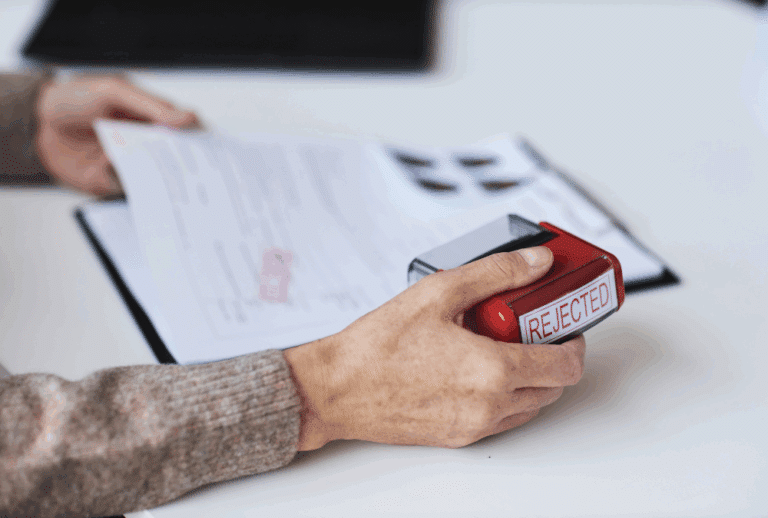 Image is of a closeup of a woman using a stamp on a claim that reads 'denied', concept of what to do if an Aiken workers' comp claim