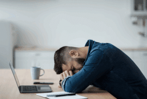 Image is of an upset man at a table with his head down while at his laptop, concept of mistakes to avoid during a personal injury claim