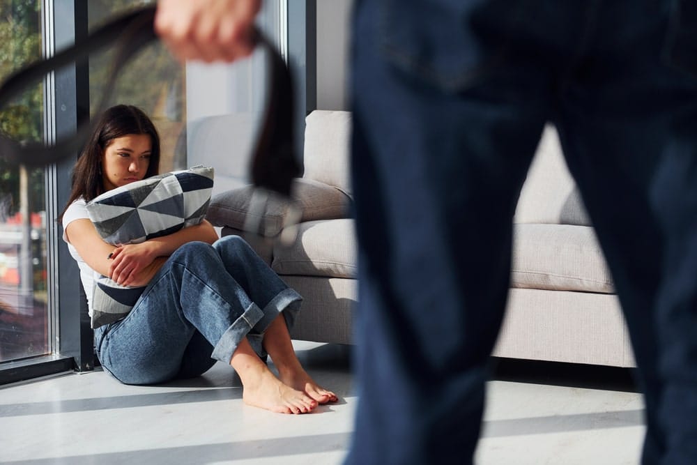 Woman sitting on the floor holding pillow as man stands nearby, showing emotional trauma and child custody in SC issues.