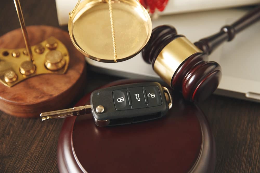 Image is of a gavel, balance scales, and a car key arranged together, concept of legal responsibility in Aiken car accident claims.