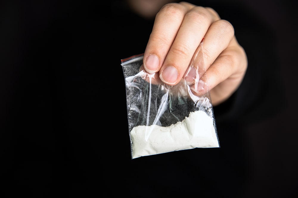 Image is of a close up hand holding a plastic bag with white powder, symbolizing controlled substance evidence in trafficking charges in SC