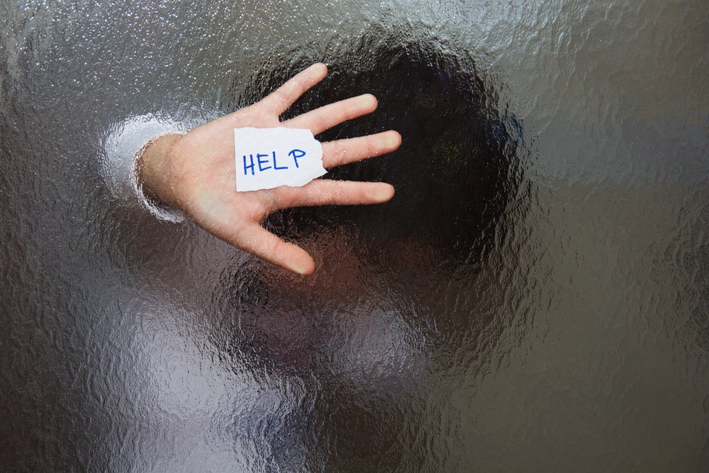 Image shows a hand pressed against frosted glass holding a note that says help, symbolizing the urgent need for intervention in domestic violence offenses in South Carolina.