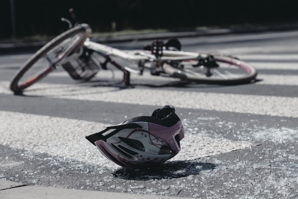 Image is of a bicycle and damaged helmet lying on a roadway after a crash, concept of determining whether you need a lawyer after a bike accident