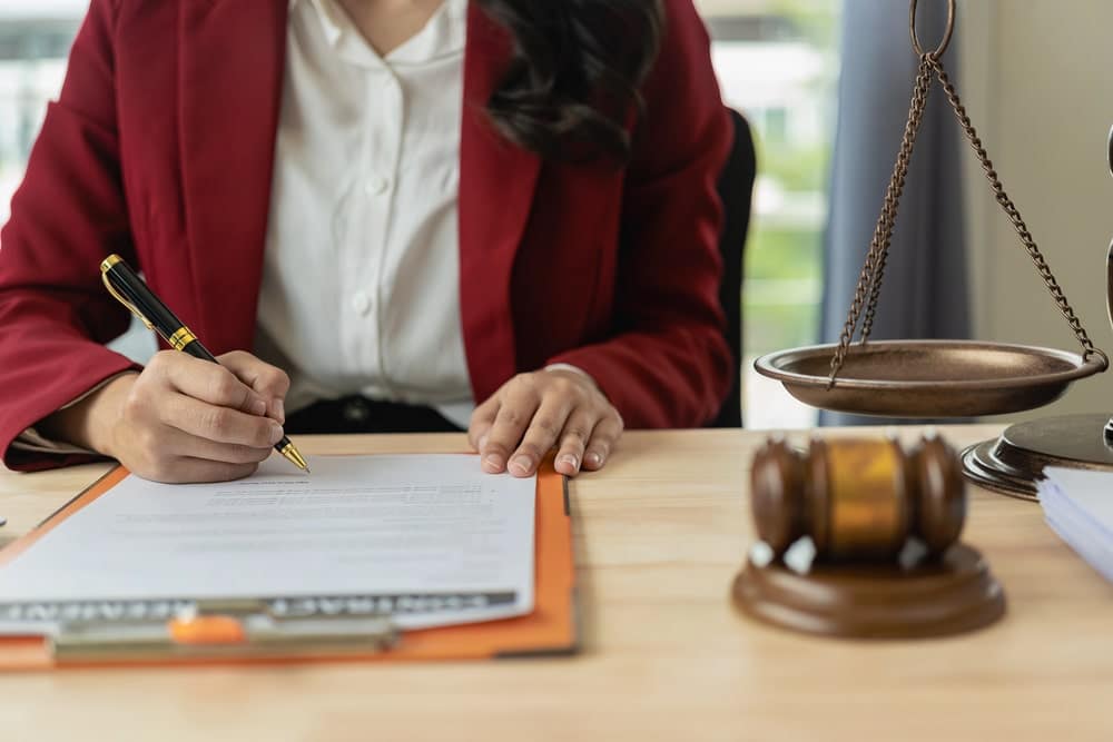 Image is of a lawyer reviewing and signing legal documents at a desk with a gavel and justice scales, concept of whether you need a lawyer after a minor car accident