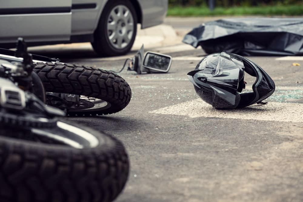 Image is of a motorcycle helmet and scattered debris on the roadway after a collision, representing the impact forces and injury risks commonly associated with motorcycle accidents.