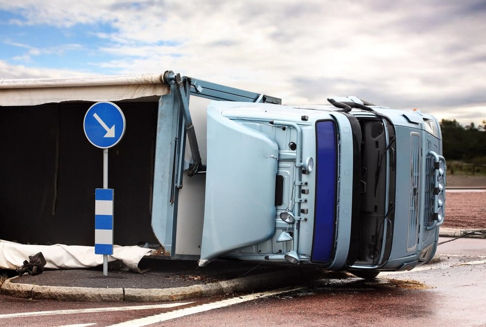 Image shows a large truck overturned on the side of the road near a traffic sign, representing the severe crashes often involved in truck accidents in SC.