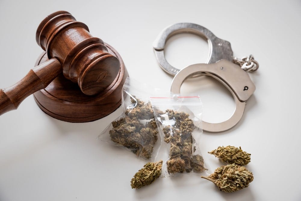 Image is of a court gavel with handcuffs and packaged marijuana, concept of drug charges involving college students