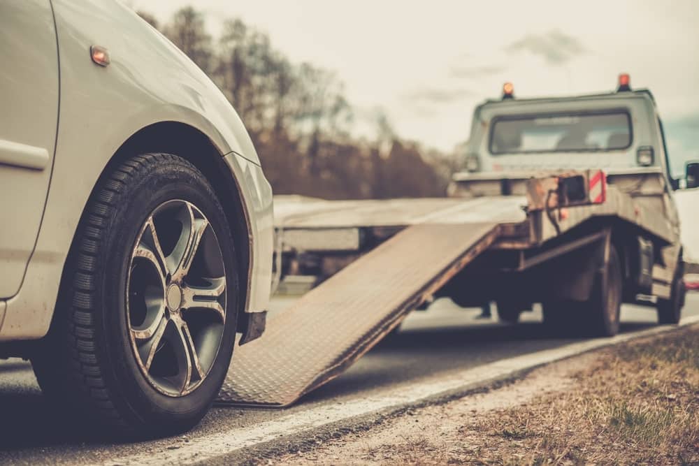 Image is of a damaged passenger vehicle being loaded onto a tow truck after a roadway collision, illustrating the aftermath and recovery process in truck accidents