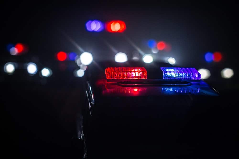 Image is of police emergency lights during a nighttime traffic stop, representing law enforcement encounters and search considerations in South Carolina drug cases.
