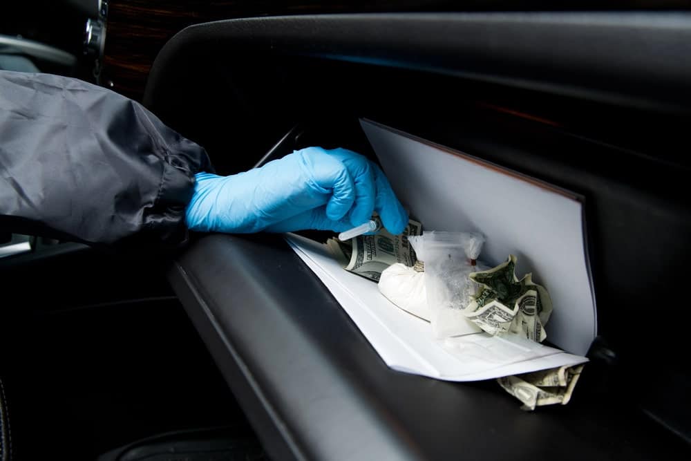 Image is of a police officer wearing gloves searching a vehicle glove compartment, concept of evidence discovery and search authority in South Carolina drug cases.