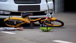 Image shows a damaged bicycle and helmet under a vehicle, emphasizing collision impact and injury outcomes in bike accidents