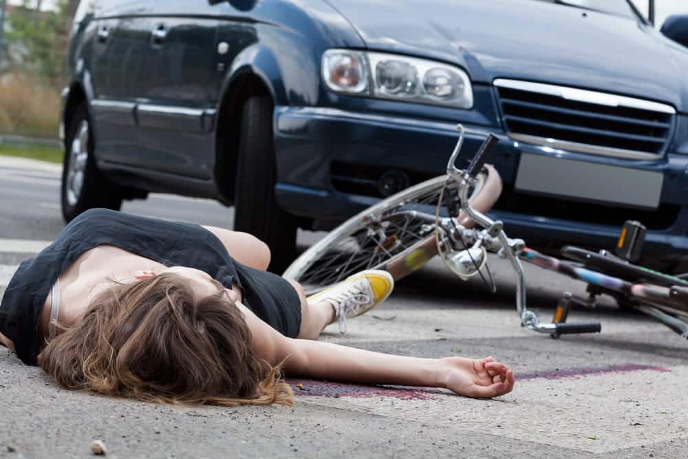 Image shows a cyclist lying on the roadway near a vehicle, illustrating serious physical trauma that can occur in bike accidents