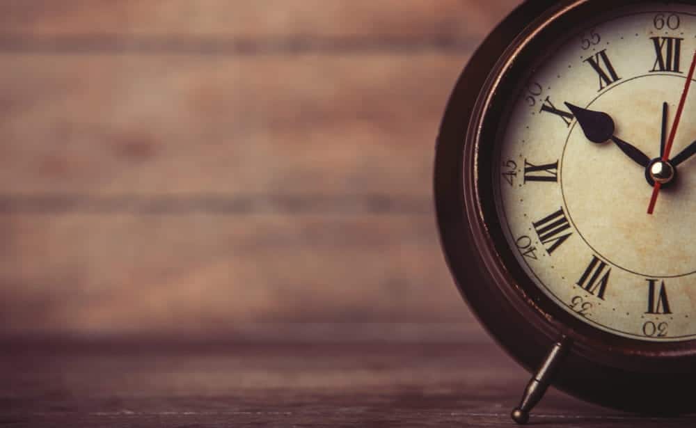 Image is of a vintage clock on a wooden surface, representing legal deadlines and timing when deciding how to sue a trucking company after a crash.