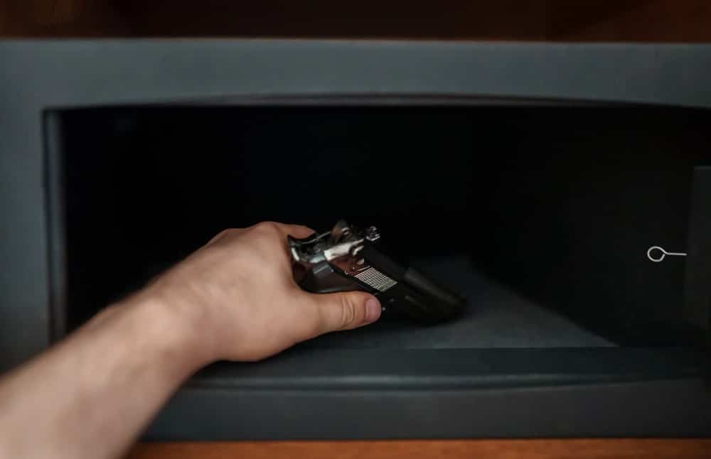 Image is of a hand placing a handgun inside a safe, illustrating firearm storage rules after domestic violence convictions