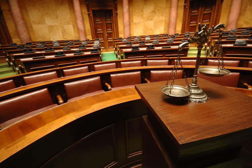 Image is of an empty courtroom with scales of justice displayed in front, representing legal proceedings after a drug arrest in Aiken.