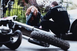 Image is of a police officer assisting an injured person near a fallen bike, showing response after a motorcycle crash