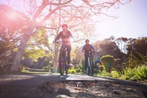 Image is of two cyclists approaching a damaged road surface with a pothole, representing poor road conditions in Aiken and potential safety risks