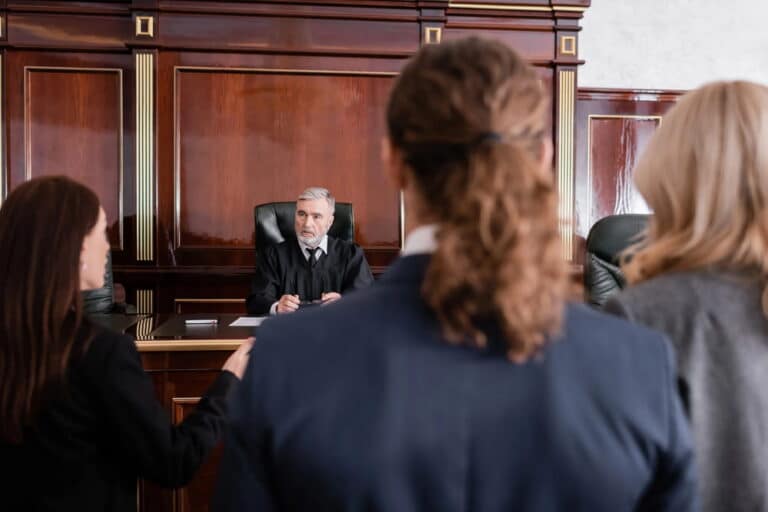 Image is of a judge speaking to individuals standing before the bench during a courtroom hearing, concept of how a judge supervises progress during a drug court appearance in Aiken.