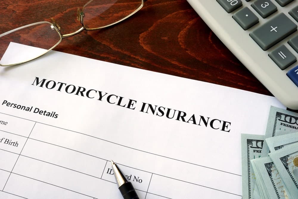 Image is of a motorcycle insurance form with cash and a pen on a desk, representing motorcycle accident insurance claims and financial coverage