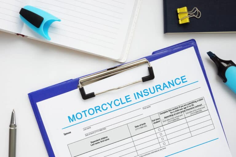 Image is of a clipboard holding a motorcycle insurance document with office supplies, concept of motorcycle accident insurance paperwork and claim filing process